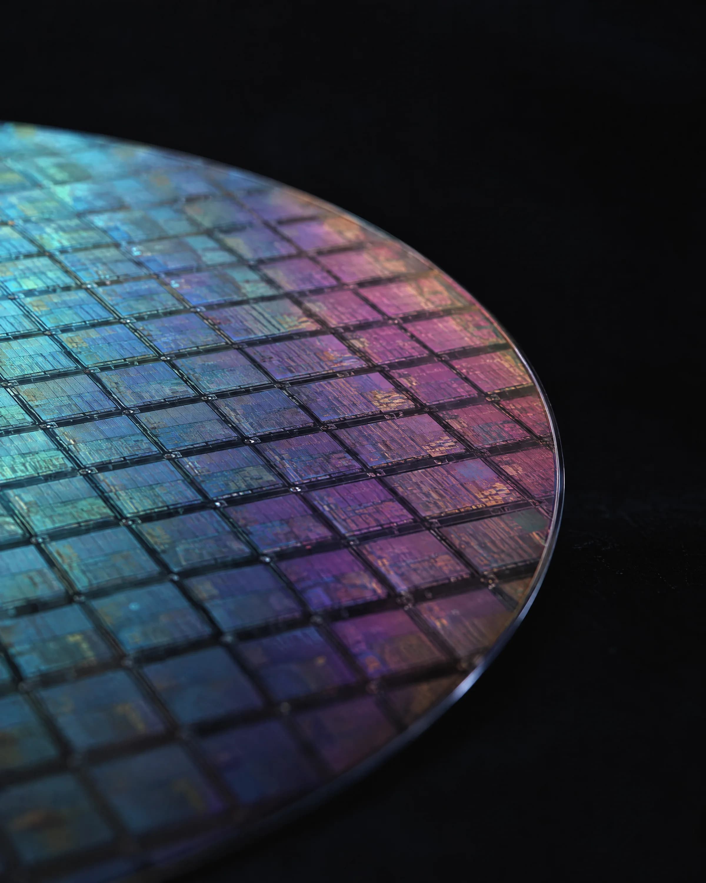 A silicon wafer with iridescent cyan and violet chip dies on black.